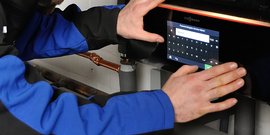Ein Techniker in blauer Arbeitskleidung bedient ein digitales Bedienfeld einer Heizungsanlage mit beiden Händen.