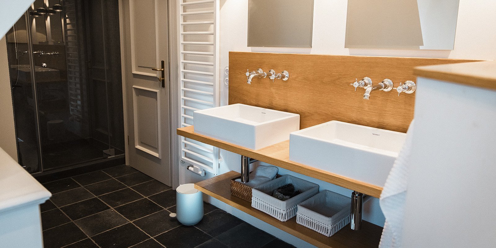 Ein modernes Badezimmer mit zwei weißen Waschbecken auf einer Holzablage und eleganten Wasserhähnen im Hintergrund.