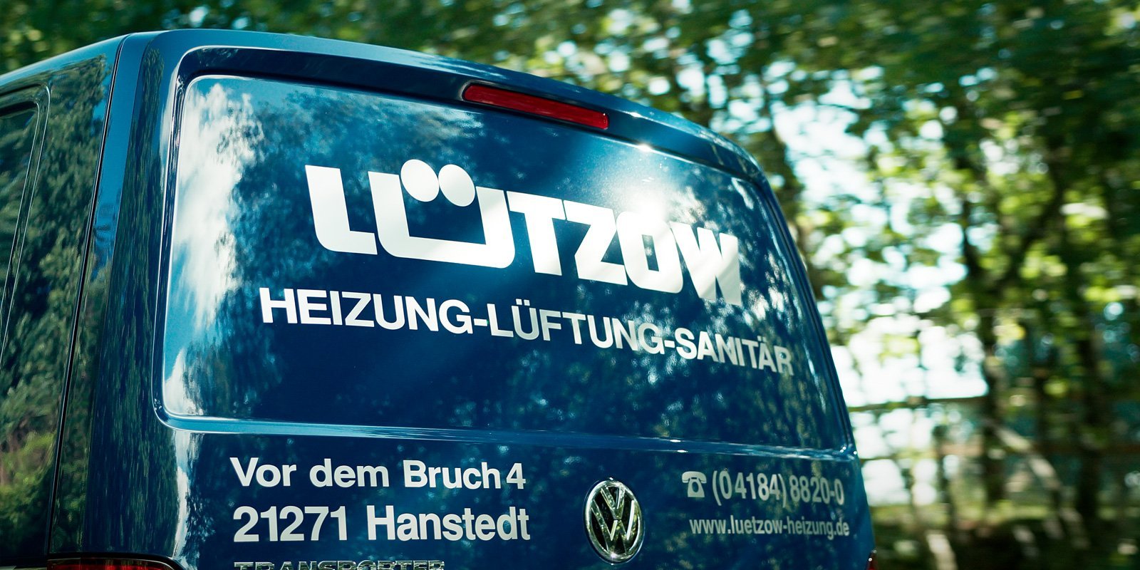 Ein blauer Lieferwagen mit dem Logo 'Lützow' und den Dienstleistungen Heizung, Lüftung, Sanitär auf der Rückseite.