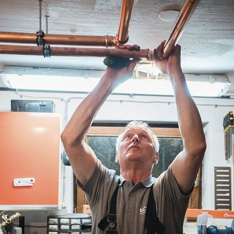 Ein Handwerker installiert Kupferrohre an der Decke einer Werkstatt, konzentriert und mit einem Werkzeug in der Hand.