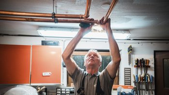 Ein Handwerker installiert Kupferrohre an der Decke einer Werkstatt, konzentriert und mit einem Werkzeug in der Hand.