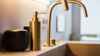 Ein eleganter Waschplatz mit goldenen Armaturen und modernen Pflegeprodukten auf einer stilvollen Oberfläche.