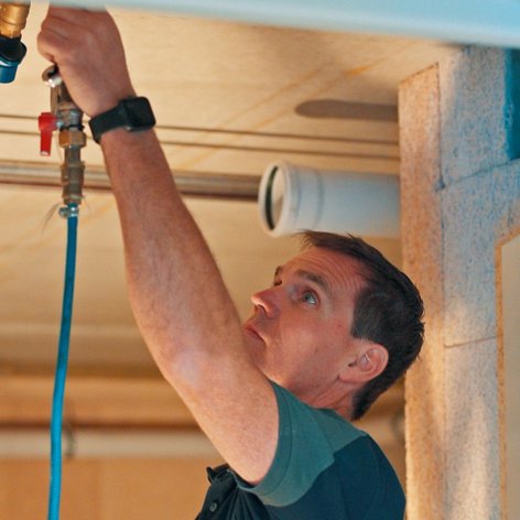 Ein Handwerker arbeitet konzentriert an Rohrleitungen, während er eine Armatur über seinem Kopf justiert.