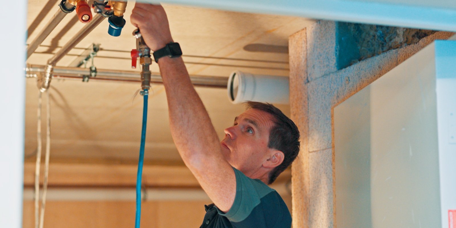 Ein Handwerker arbeitet konzentriert an Rohrleitungen, während er eine Armatur über seinem Kopf justiert.
