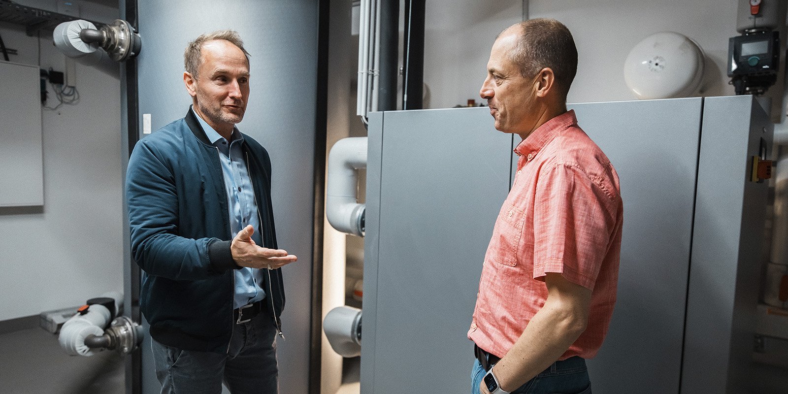 Zwei Männer stehen in einem modernen Raum und diskutieren, während sie sich gegenseitig aufmerksam ansehen.