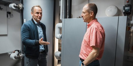 Zwei Männer stehen in einem modernen Raum und diskutieren, während sie sich gegenseitig aufmerksam ansehen.