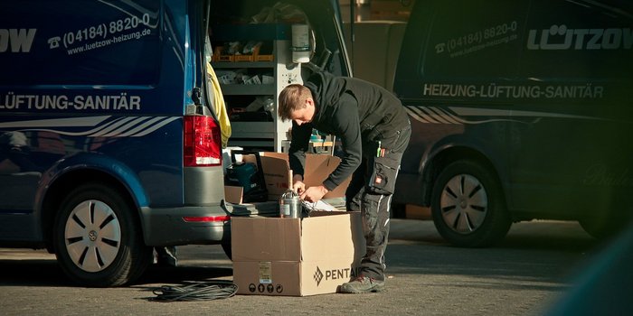 Ein Handwerker beugt sich über einen Karton, während er Werkzeuge aus einem Lieferwagen entnimmt, um seine Arbeit vorzubereiten.