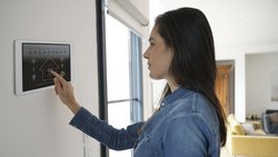 Eine Frau bedient eine Lüftung-Klima-App auf einem Display das an der Wand montiert ist, in einem Wohnzimmer.